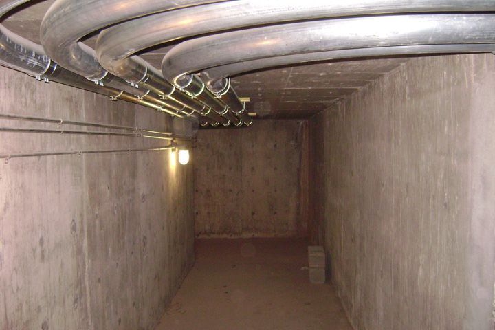 A concrete tunnel with a lot of pipes hanging from the ceiling.
