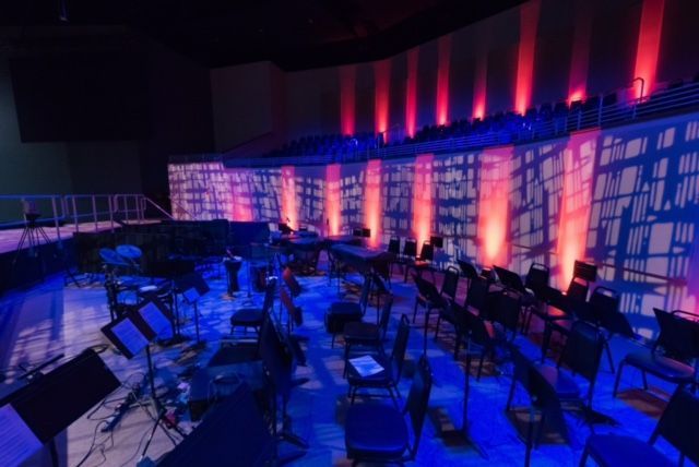 A large orchestra is sitting on a stage in a dark room.