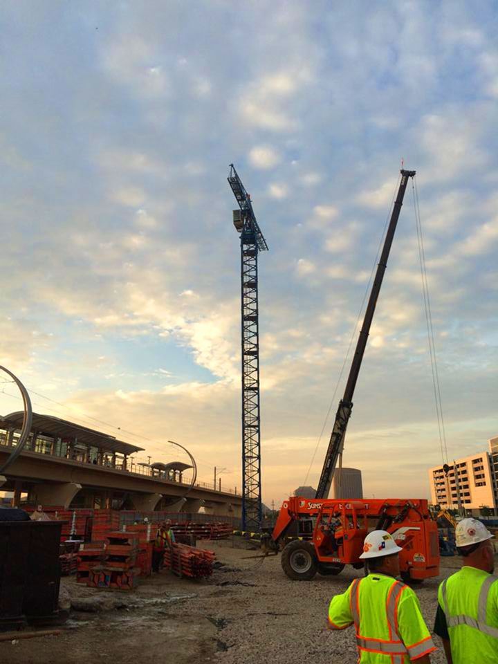 Two construction workers are standing in front of a large crane on a construction site.