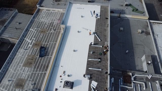 An aerial view of a white roof being installed on a building.