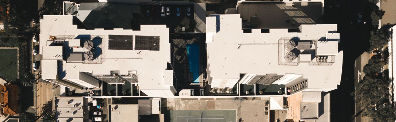 An aerial view of a large white building with a tennis court in the background.