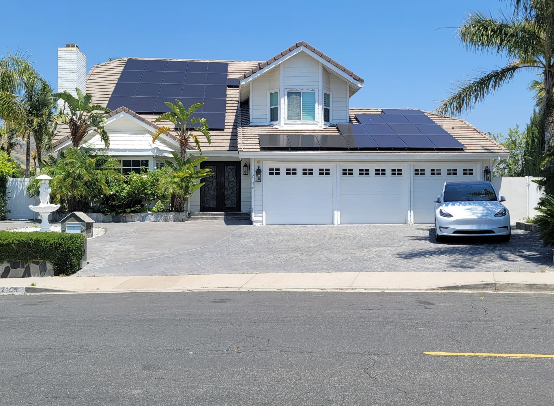 A white car is parked in front of a house with solar panels on the roof.