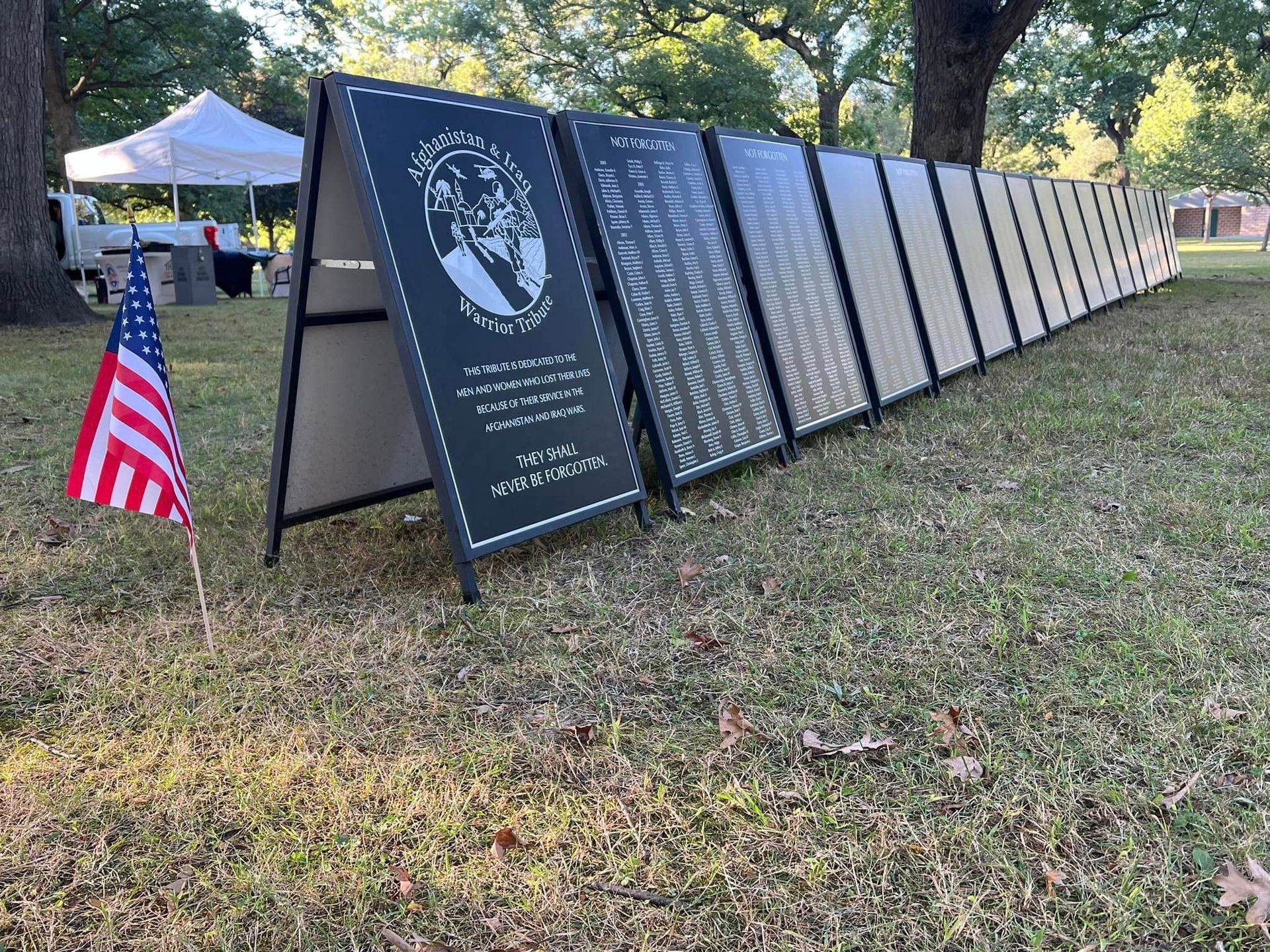 A row of signs sitting on top of a lush green field next to an american flag.