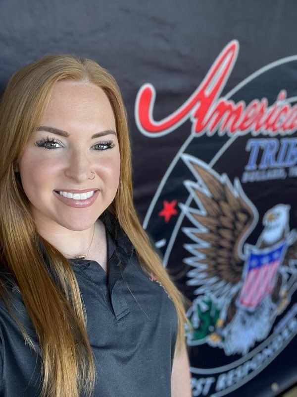 A woman is smiling in front of an american tribe banner