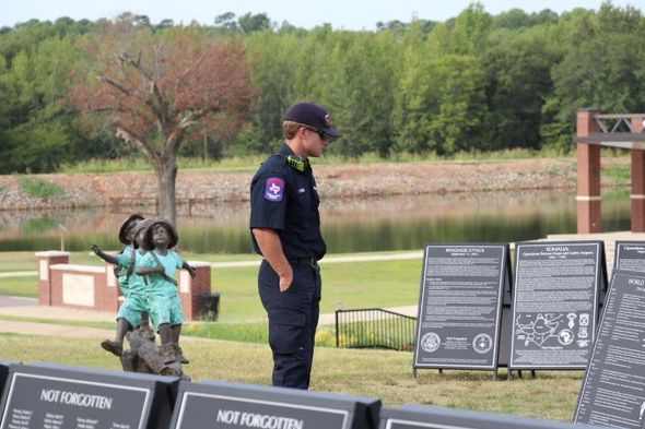 A police officer is standing in front of a memorial with plaques that say not forgotten.