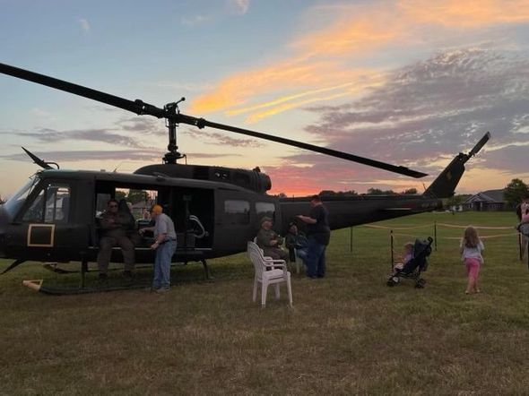 A helicopter is parked in a grassy field with people standing around it.