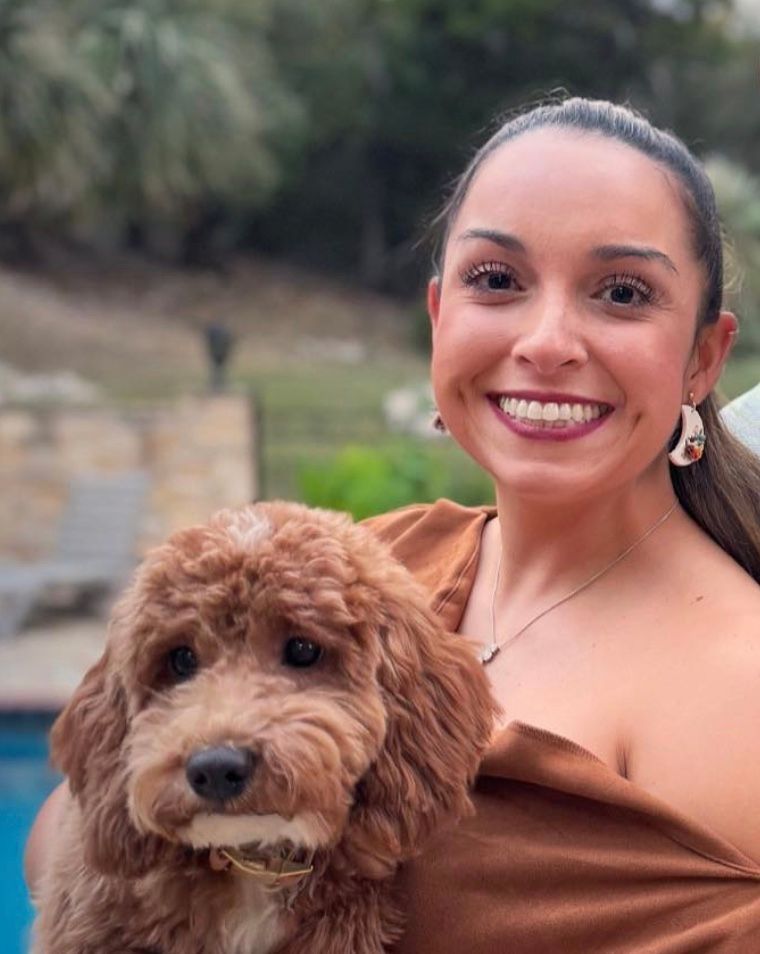 A woman wearing a black top and a white sweater is smiling for the camera.