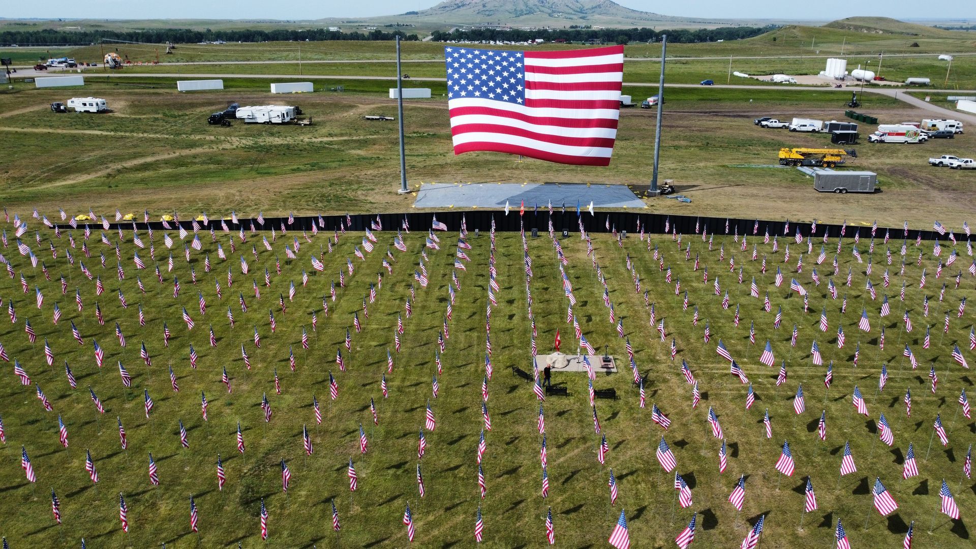 A large american flag is flying over a field of american flags.