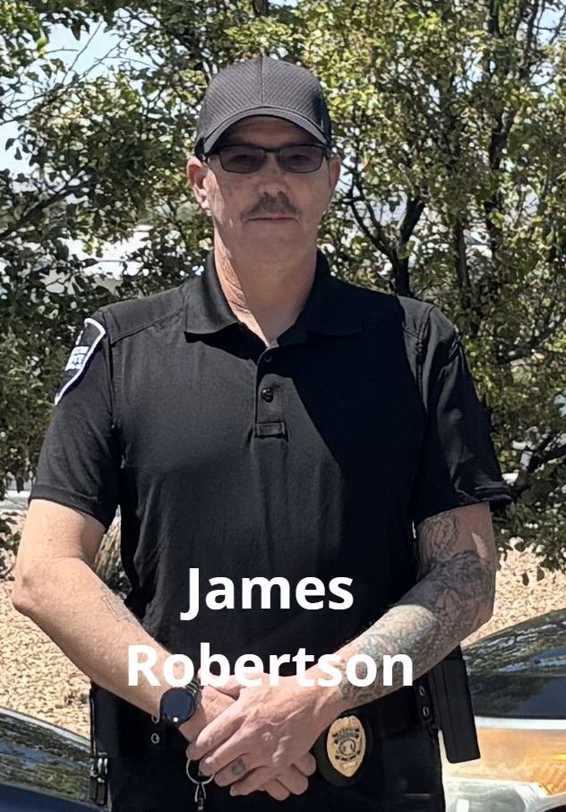 A man in a black uniform and cap, James Robertson, stands outdoors. He has sunglasses and a tattoo on his arm.