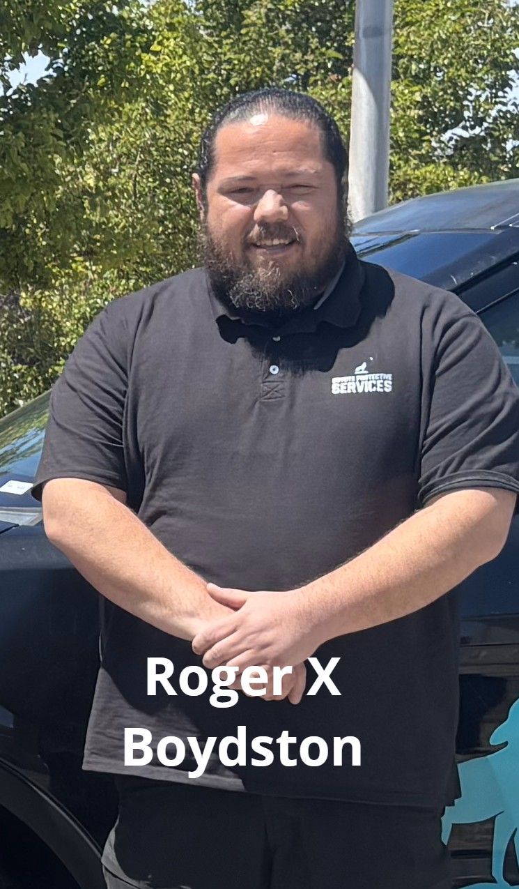 Roger X Boydston, a man with a beard, in a black polo shirt, standing outdoors.