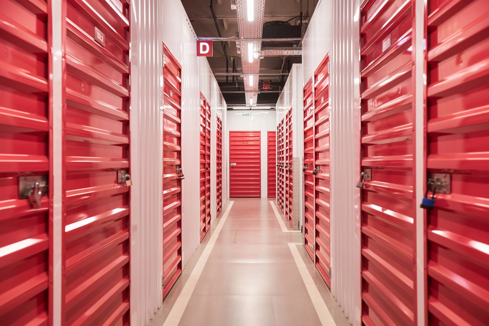 Red storage unit hallway, metal doors, bright overhead lights.
