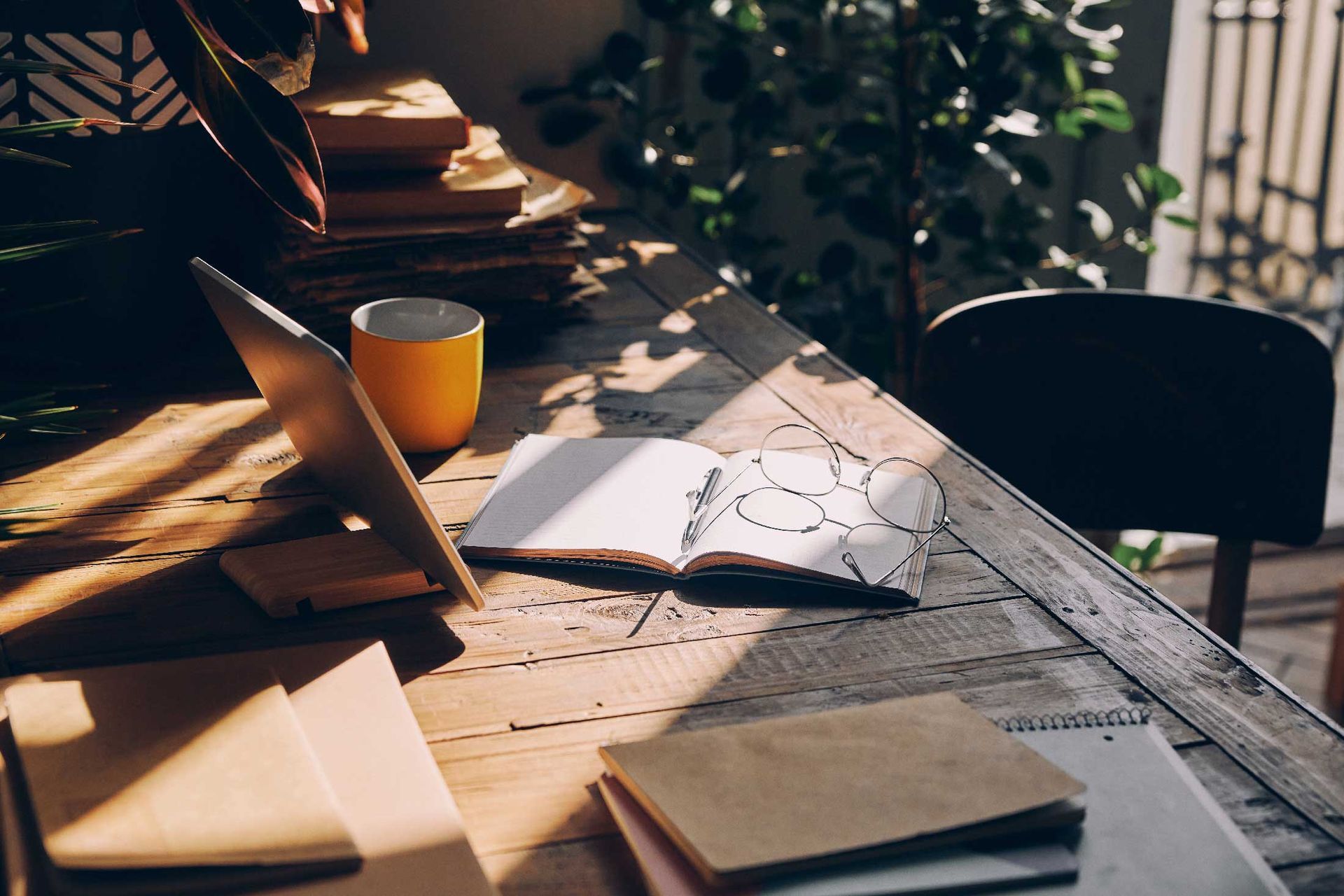 A wooden desk with a laptop , notebooks , and a cup of coffee.