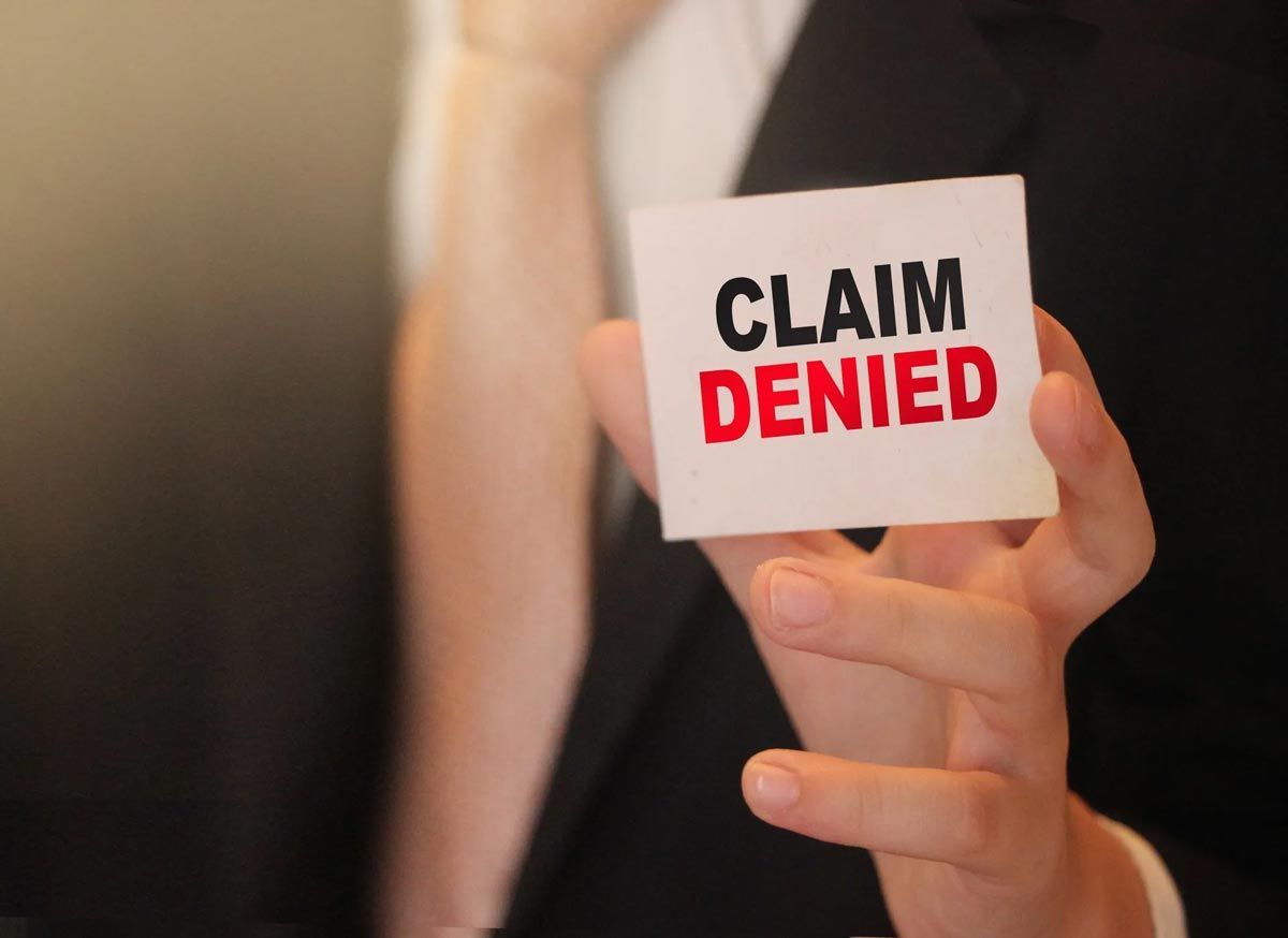 Person holding a “CLAIM DENIED” card, symbolizing rejected insurance or benefits request