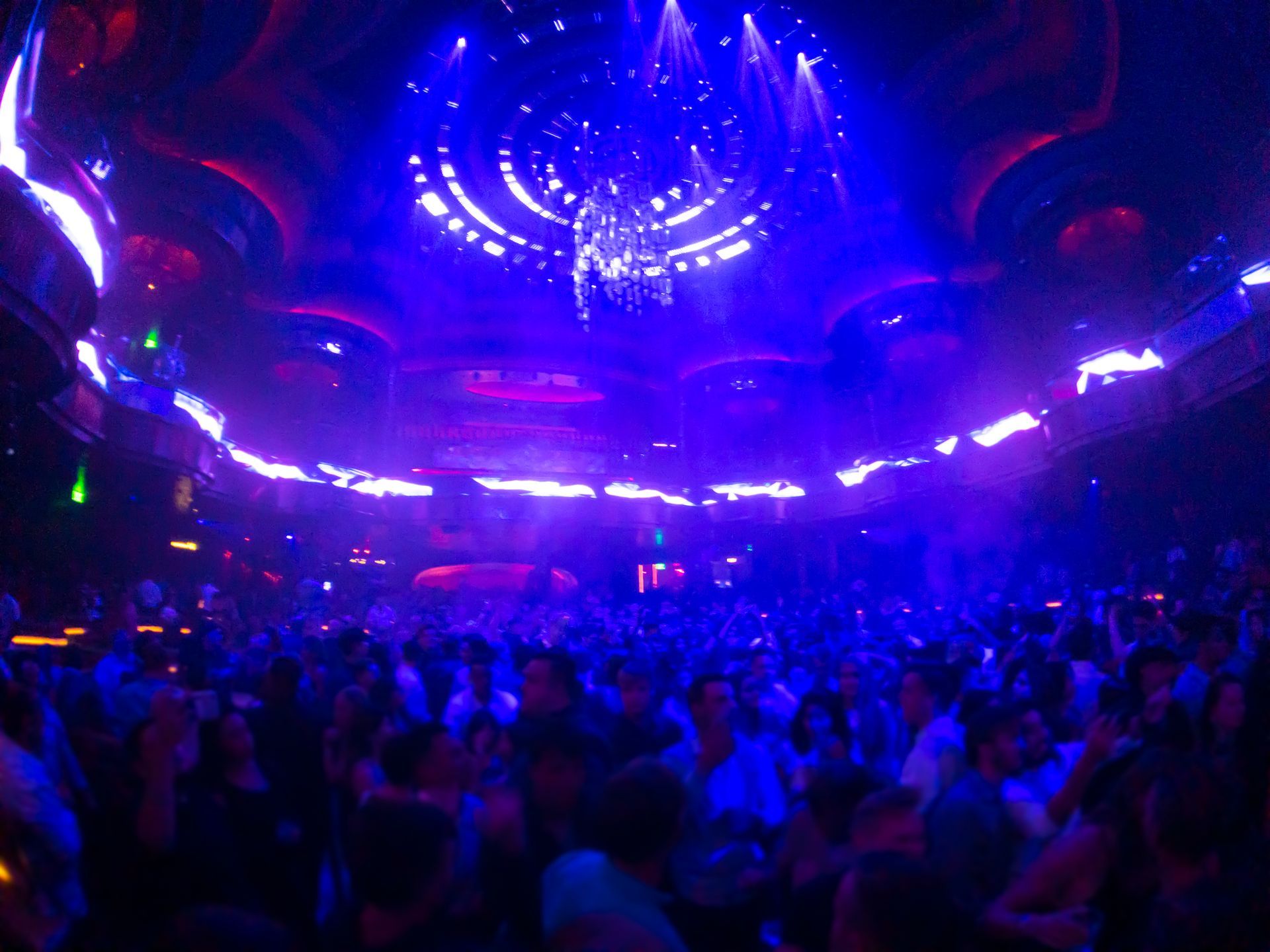 Crowded nightclub with vibrant blue and purple lights above a dancing crowd.