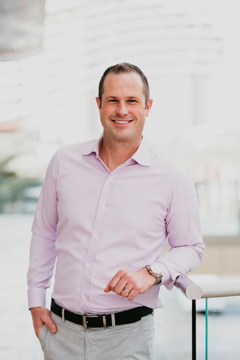 A man in a pink shirt and gray pants is standing next to a table.