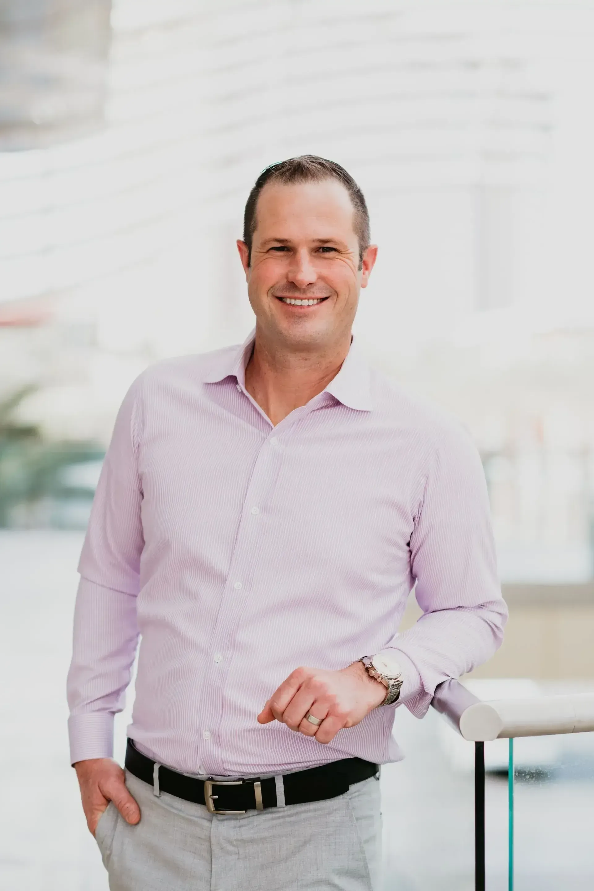 A man in a pink shirt and gray pants is standing next to a table.