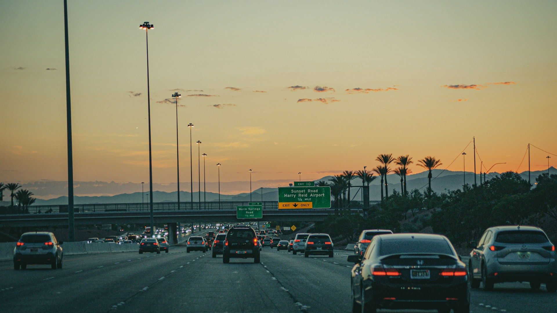Evening traffic on a Las Vegas highway with airport exit signs at sunset.
