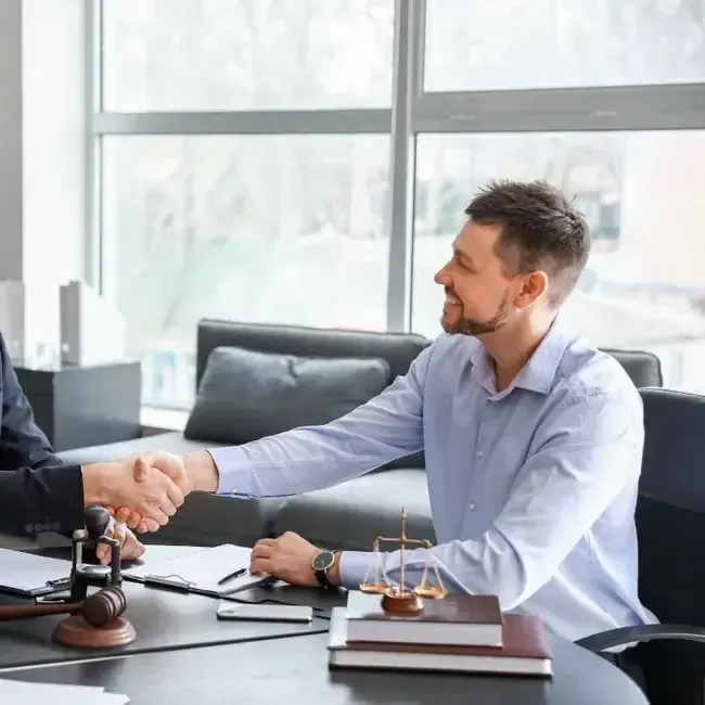 Two men are shaking hands while sitting at a table.