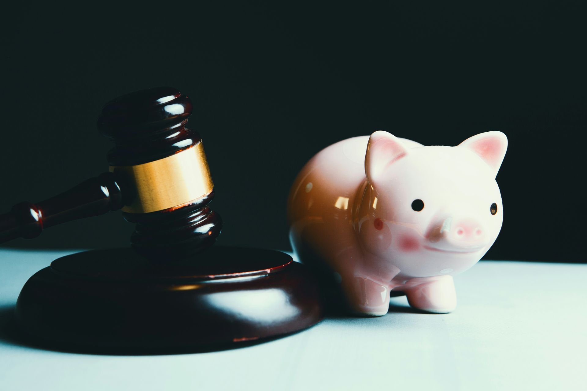 Judge’s gavel beside a pink piggy bank, representing the financial impact of legal proceedings.