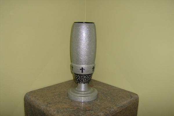 A silver vase with a cross on it is sitting on a table.