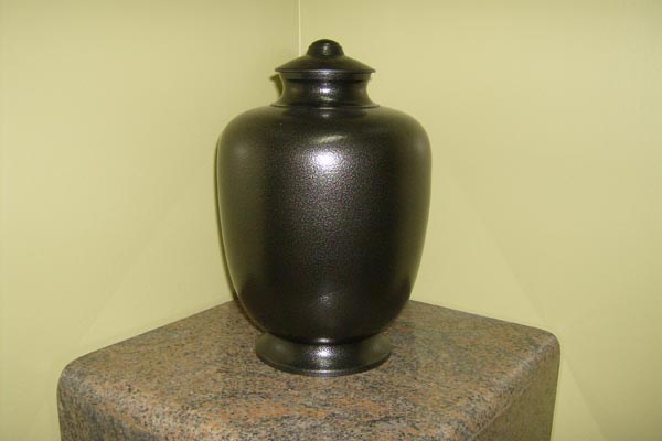 A black vase with a lid is sitting on top of a granite table.