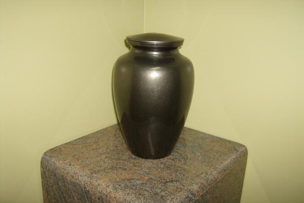 A black vase is sitting on top of a granite pedestal.
