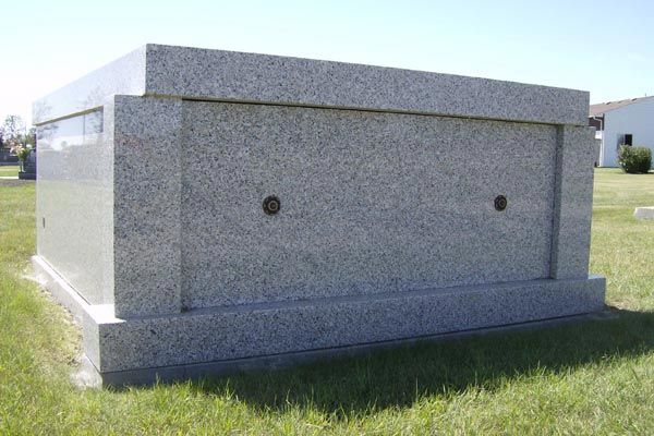 A large grave in a cemetery with a white building in the background.