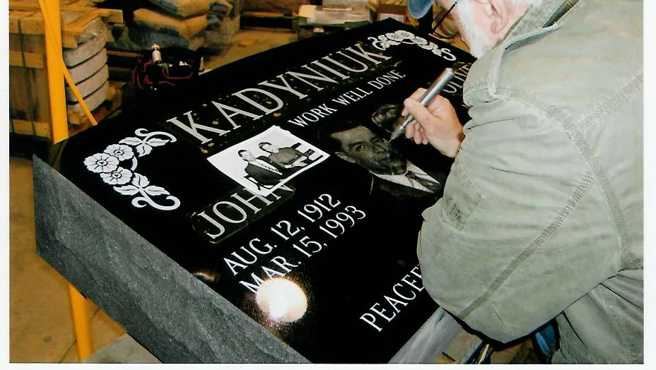 A man is writing on a gravestone for john kadyniuk