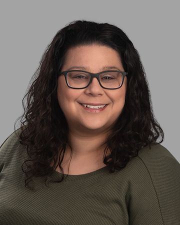 A woman wearing glasses and a green shirt is smiling for the camera.