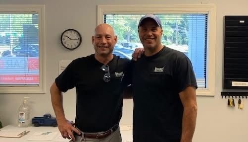 Two men are standing next to each other in a room with a clock on the wall.