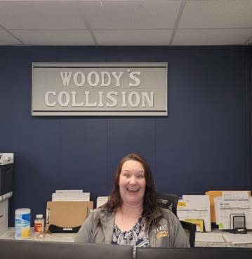 A woman sits at a desk under a woody 's collision sign