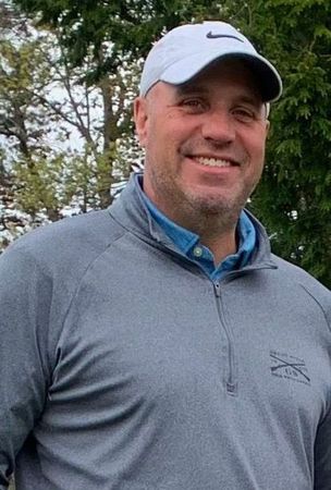 A man wearing a hat and a gray shirt is smiling for the camera.