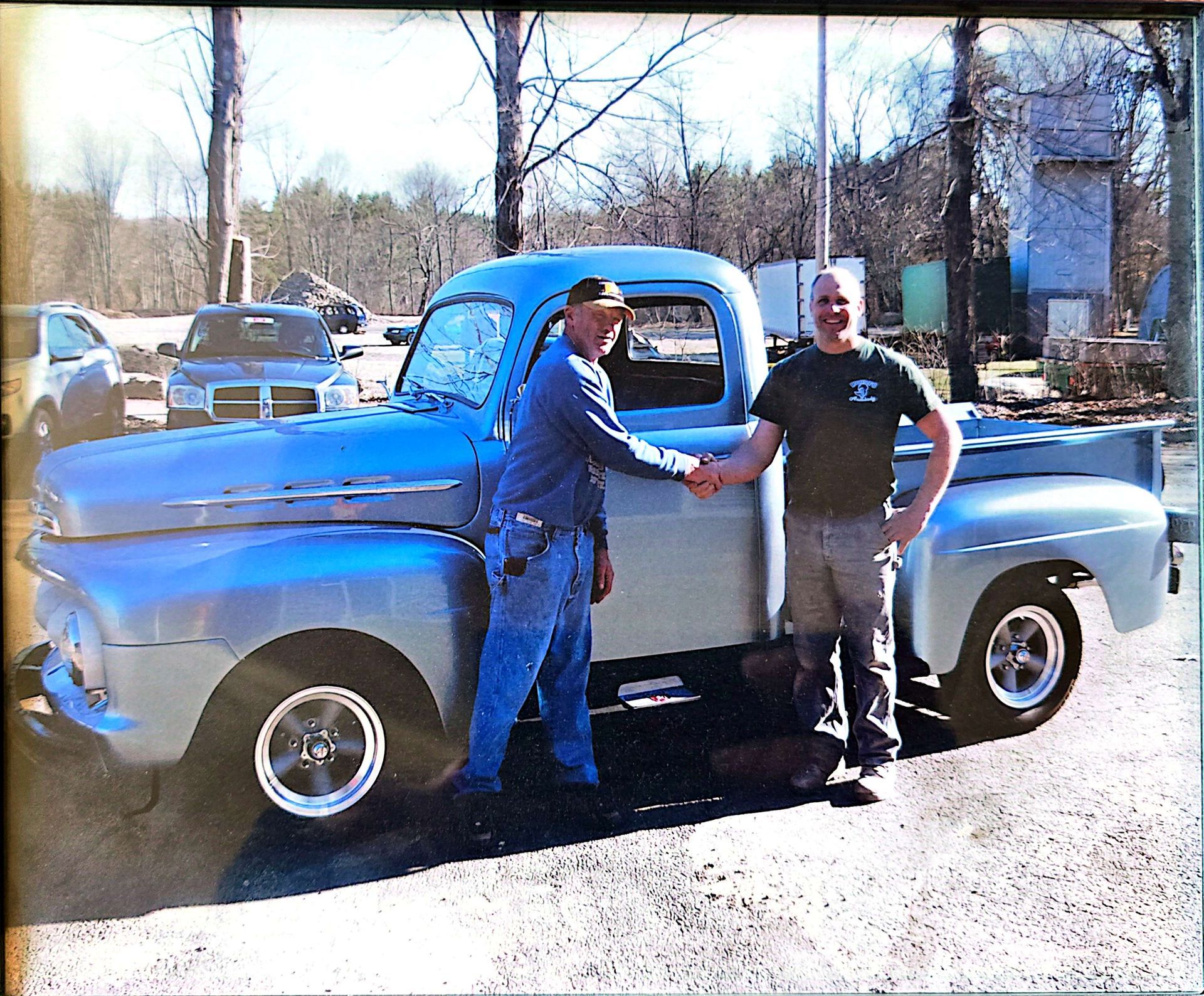 Two men shaking hands in front of a blue truck
