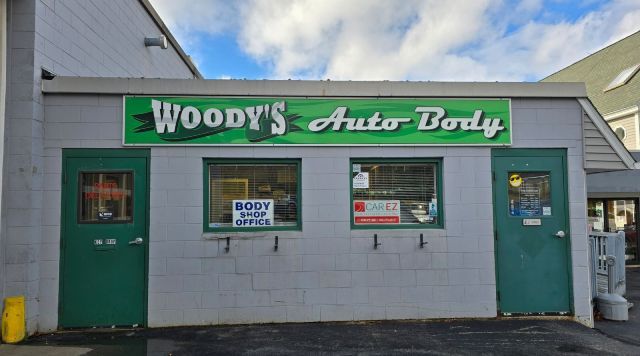 A building with a green sign that says woody 's auto body