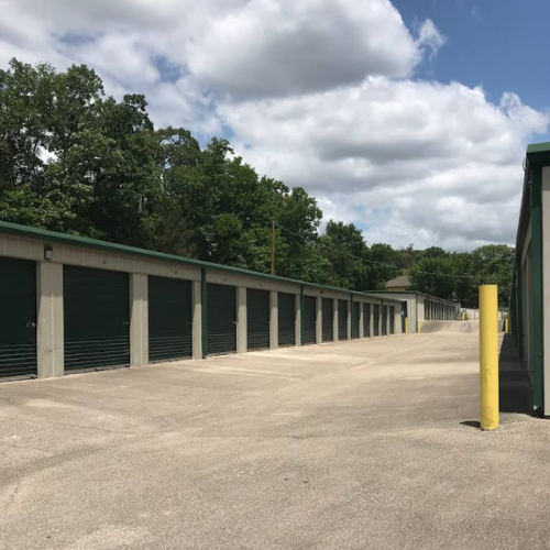 Three blue storage unit doors with white numbers 7, 8, and 9. Yellow bollards separate each door.