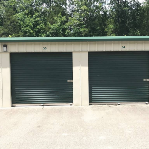 Warehouse interior with tall orange shelving stacked with cardboard boxes. Exit door at the end of the aisle.