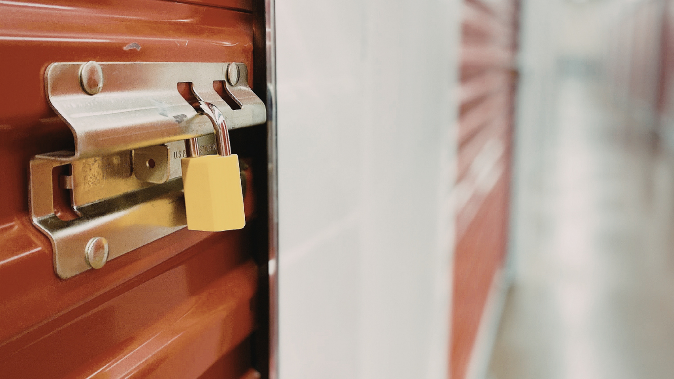 Close-up of a storage unit door with a yellow padlock, in a hallway of similar units.