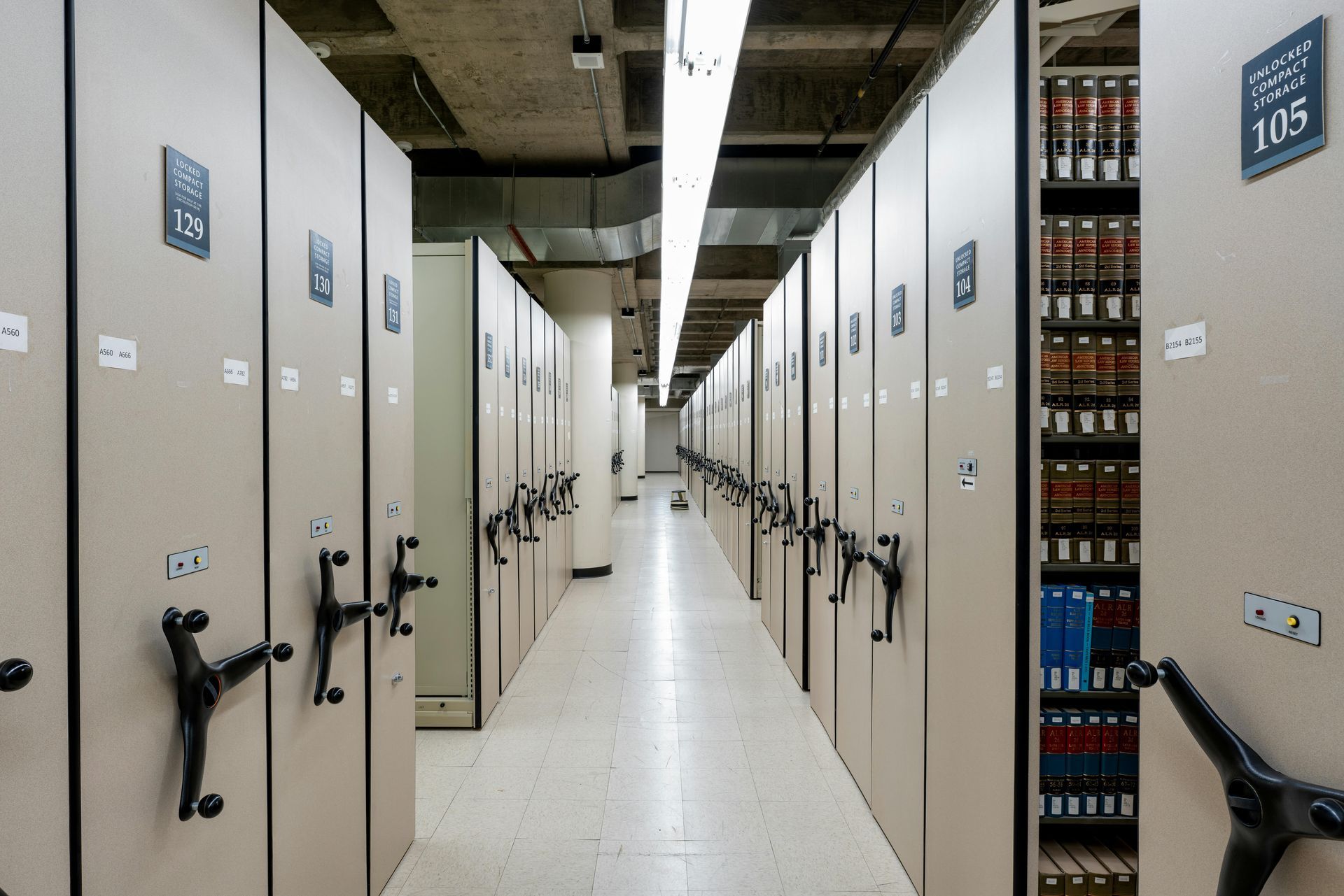 Row of tall, beige shelving units in a storage room; some units hold books.