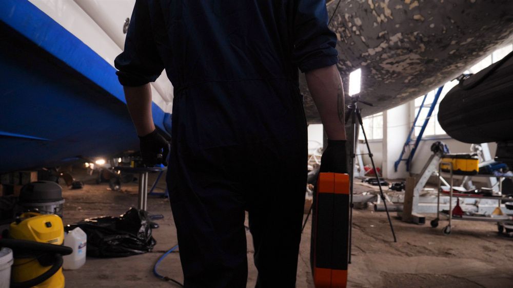 A Man Is Working On A Boat In A Garage — Mark's Outboards & More
 In Maitland, NSW