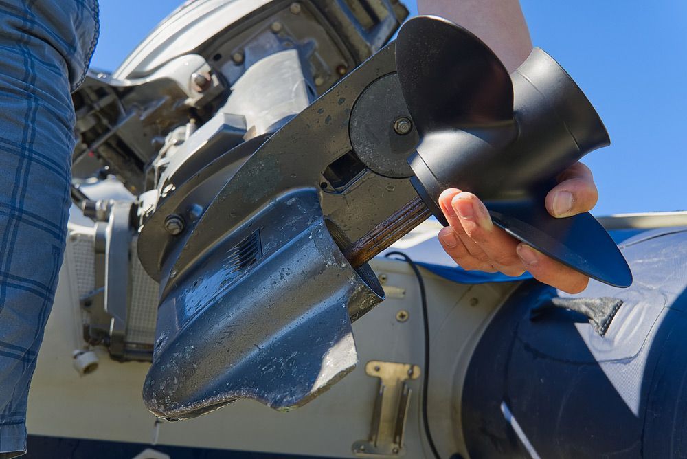 A Person Is Holding A Propeller Next To A Boat Engine — Mark's Outboards & More In Cessnock, NSW