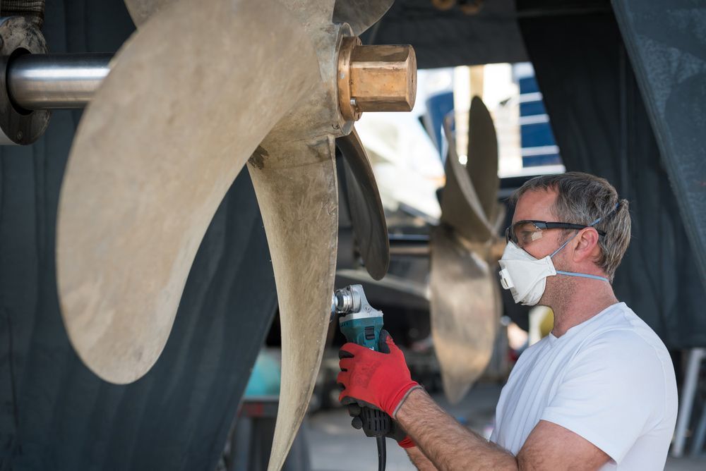 A Man Wearing A Mask Is Working On A Boat Propeller — Mark's Outboards & More In Port Stephens, NSW