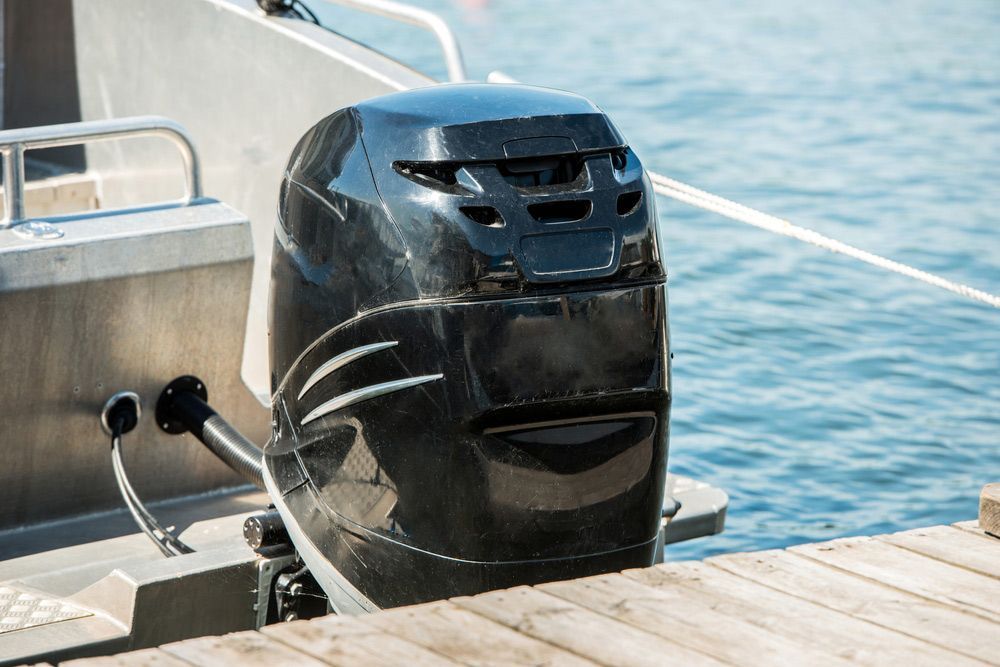 A Boat Engine Is Sitting On A Dock Next To The Water — Mark's Outboards & More In Muswellbrook, NSW