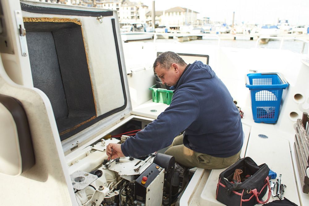 A Man Is Working On The Engine Of A Boat — Mark's Outboards & More In Newcastle, NSW