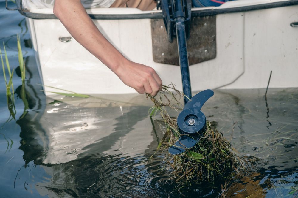 A Person Is Cleaning The Propeller Of A Boat In The Water — Mark's Outboards & More In Port Stephens, NSW
