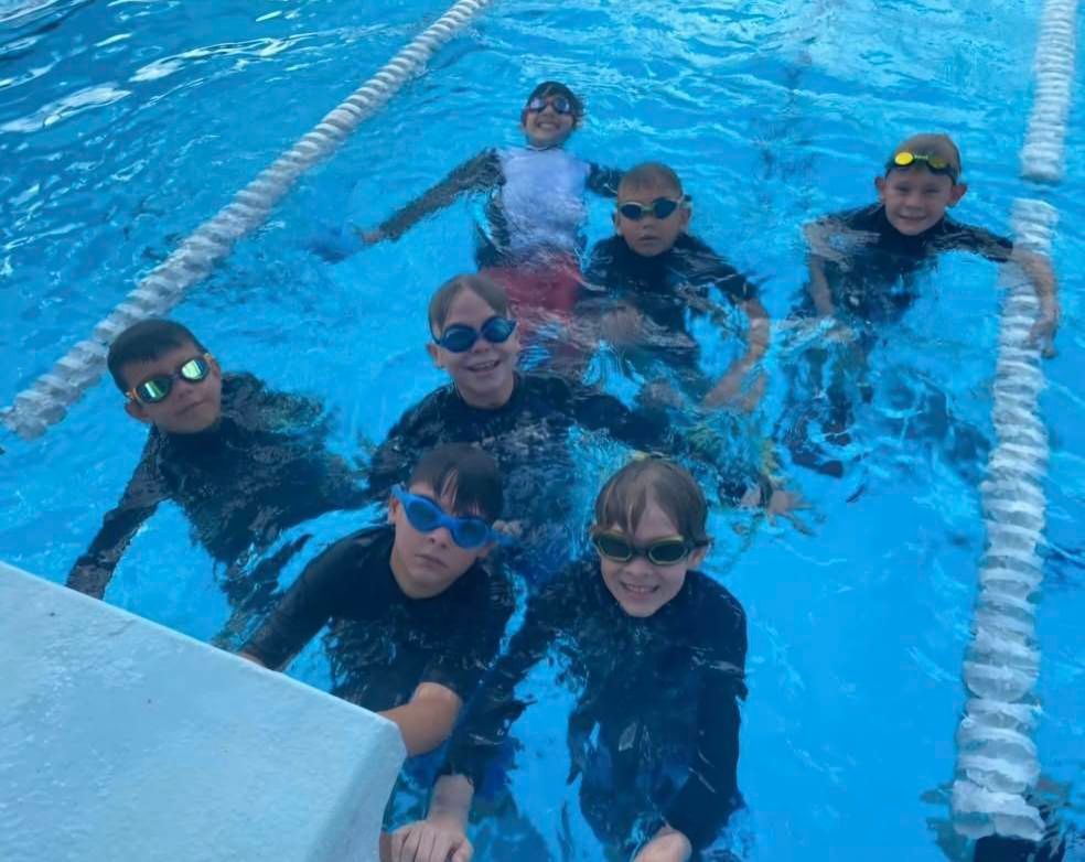 Children in a pool, wearing goggles and swim shirts, smiling and looking at the camera. — DNA Aquatics in Bundaberg, QLD