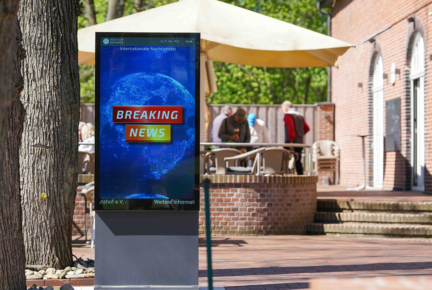 Auf einem sonnigen, grünen Fairway steht eine Golftasche neben einem hohen, vertikalen digitalen Anzeigetafel, die Informationen anzeigt.