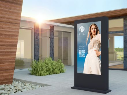 Auf einer digitalen Werbetafel ist ein Model in weißer Kleidung und ein QR-Code zu sehen, das auf einem sonnigen Platz im Freien steht.