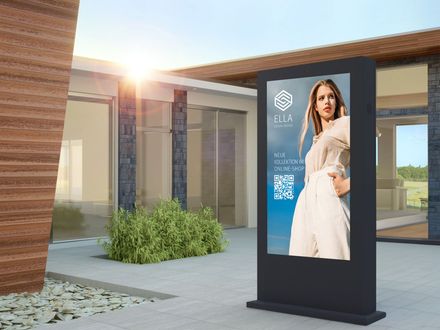 Auf einer digitalen Werbetafel ist ein Model in weißer Kleidung und ein QR-Code zu sehen, das auf einem sonnigen Platz im Freien steht.