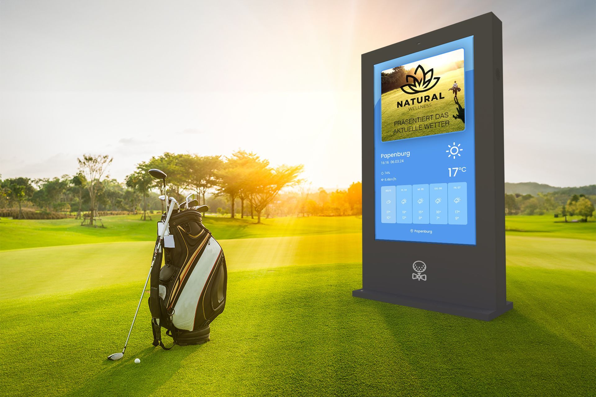 Auf einem sonnigen, grünen Fairway steht eine Golftasche neben einem hohen, vertikalen digitalen Anzeigetafel, die Informationen anzeigt.