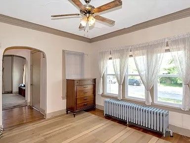 A living room with a ceiling fan , radiator , dresser and windows.